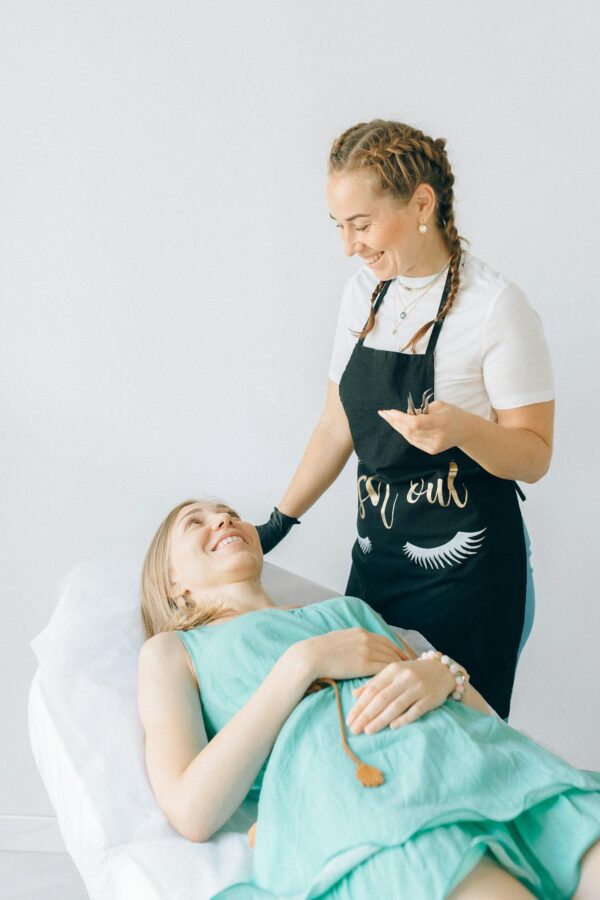 Beautician in apron engages with smiling client in bright spa environment, conveying relaxation.