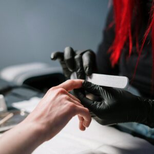 Close-up of a professional manicurist providing nail care with black gloves.