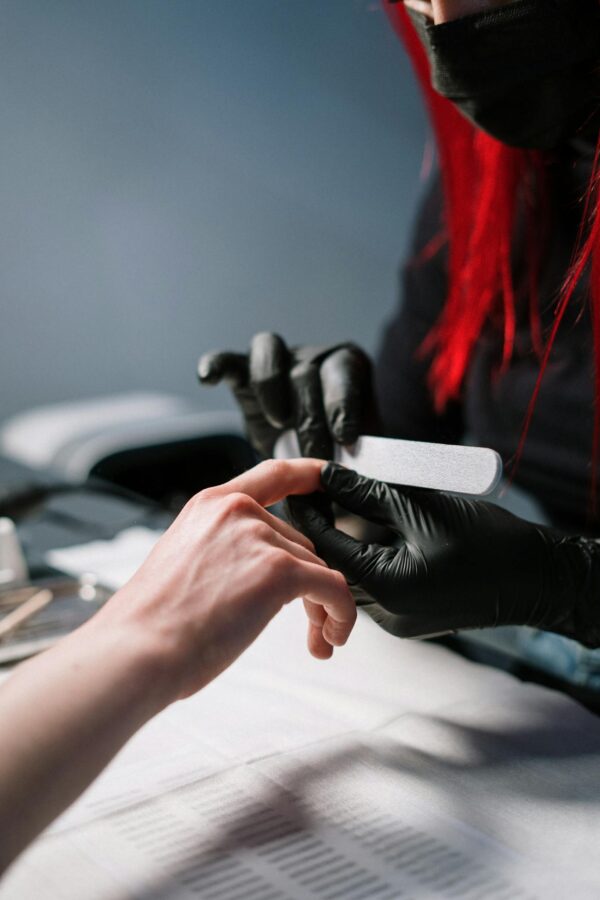 Close-up of a professional manicurist providing nail care with black gloves.